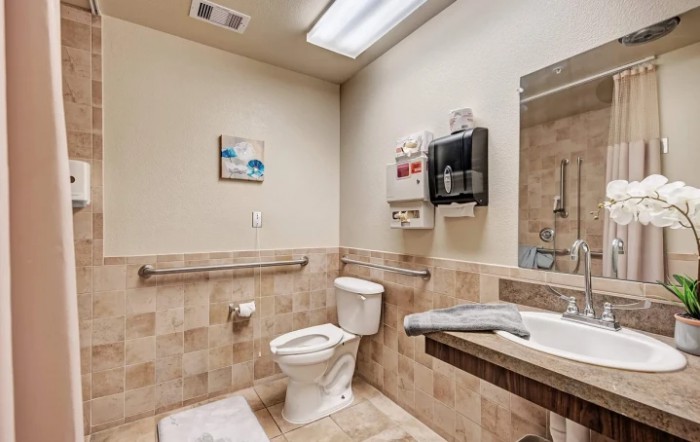 A clean and accessible bathroom featuring a toilet, sink, hand dryer, and grab bars.