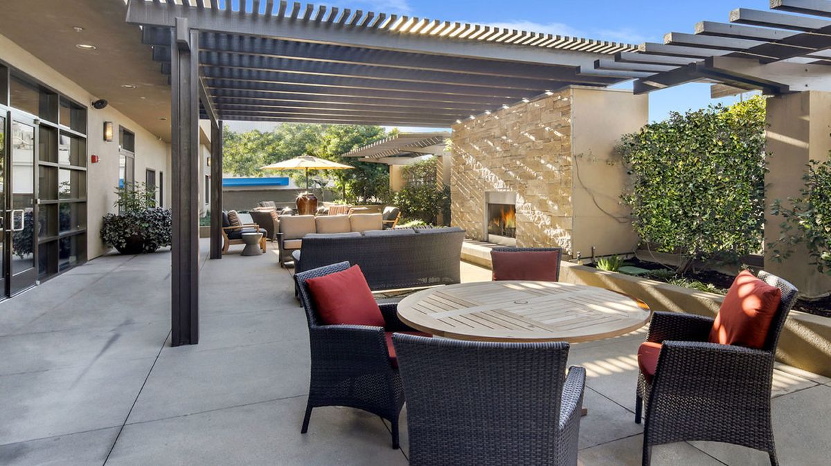 A sunny outdoor patio with comfortable seating, a pergola, and a garden view.