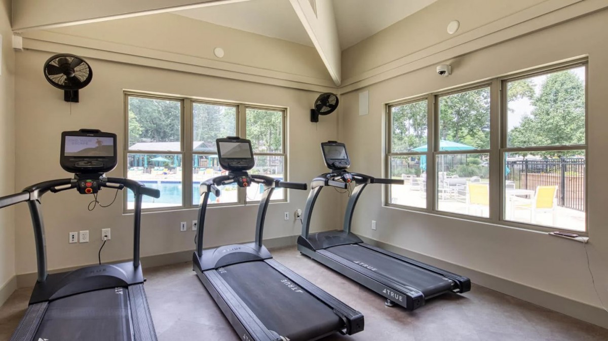A bright gym room with treadmills and large windows offering natural light.
