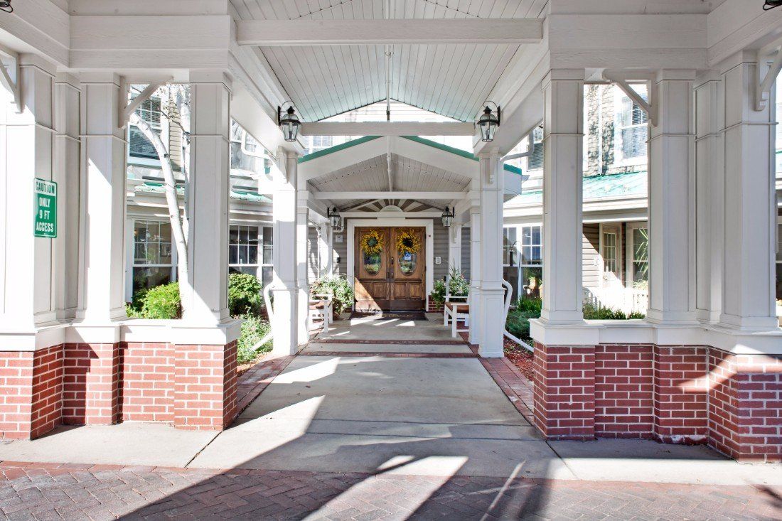 A covered entranceway leading to a building, featuring bright pillars and a brick foundation.