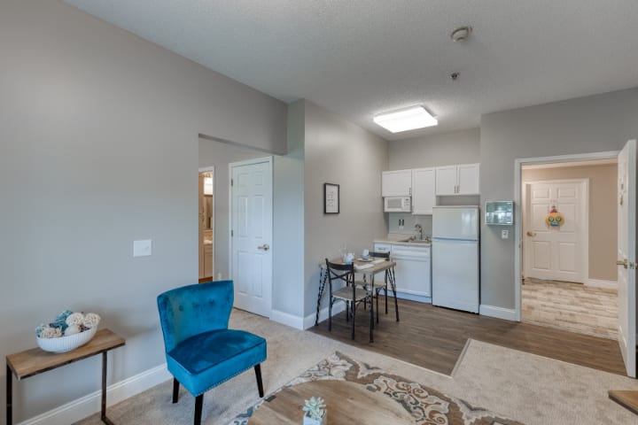 A cozy living space with a view of the kitchen, featuring a blue chair and dining table.