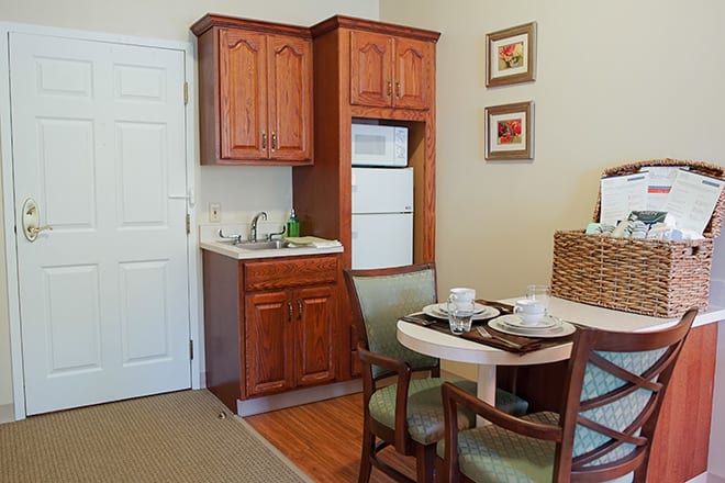 A compact kitchenette with wooden cabinets, a small dining table, and two chairs.