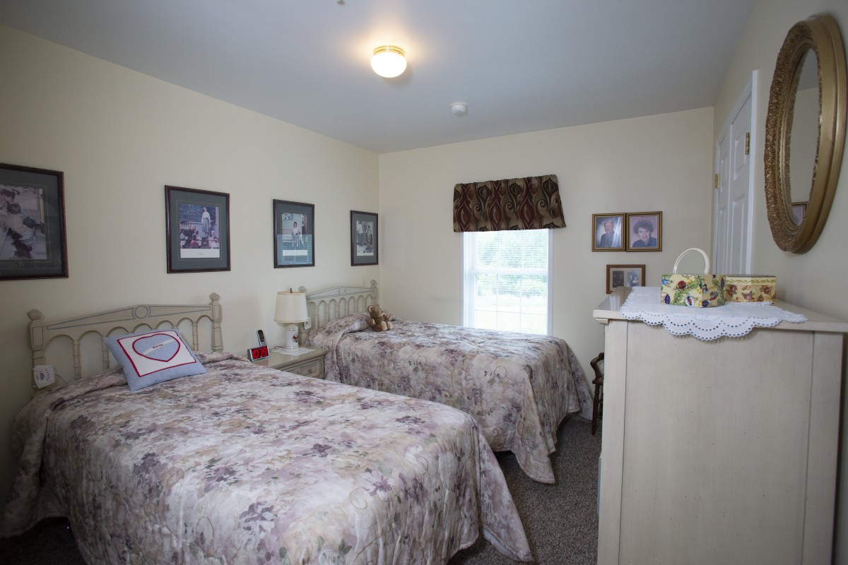 A cozy bedroom with twin beds, decorated with framed pictures and a window providing natural light.