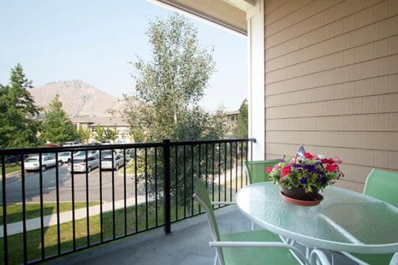 A cozy balcony with a table and chairs, adorned with a colorful potted plant overlooking a scenic view.