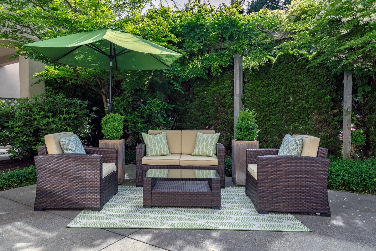 A cozy outdoor patio setup with rattan furniture and lush greenery.