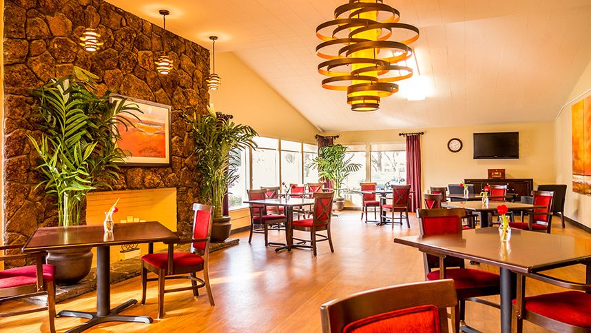 A warmly lit restaurant interior featuring elegant chandeliers and red-cushioned seating.