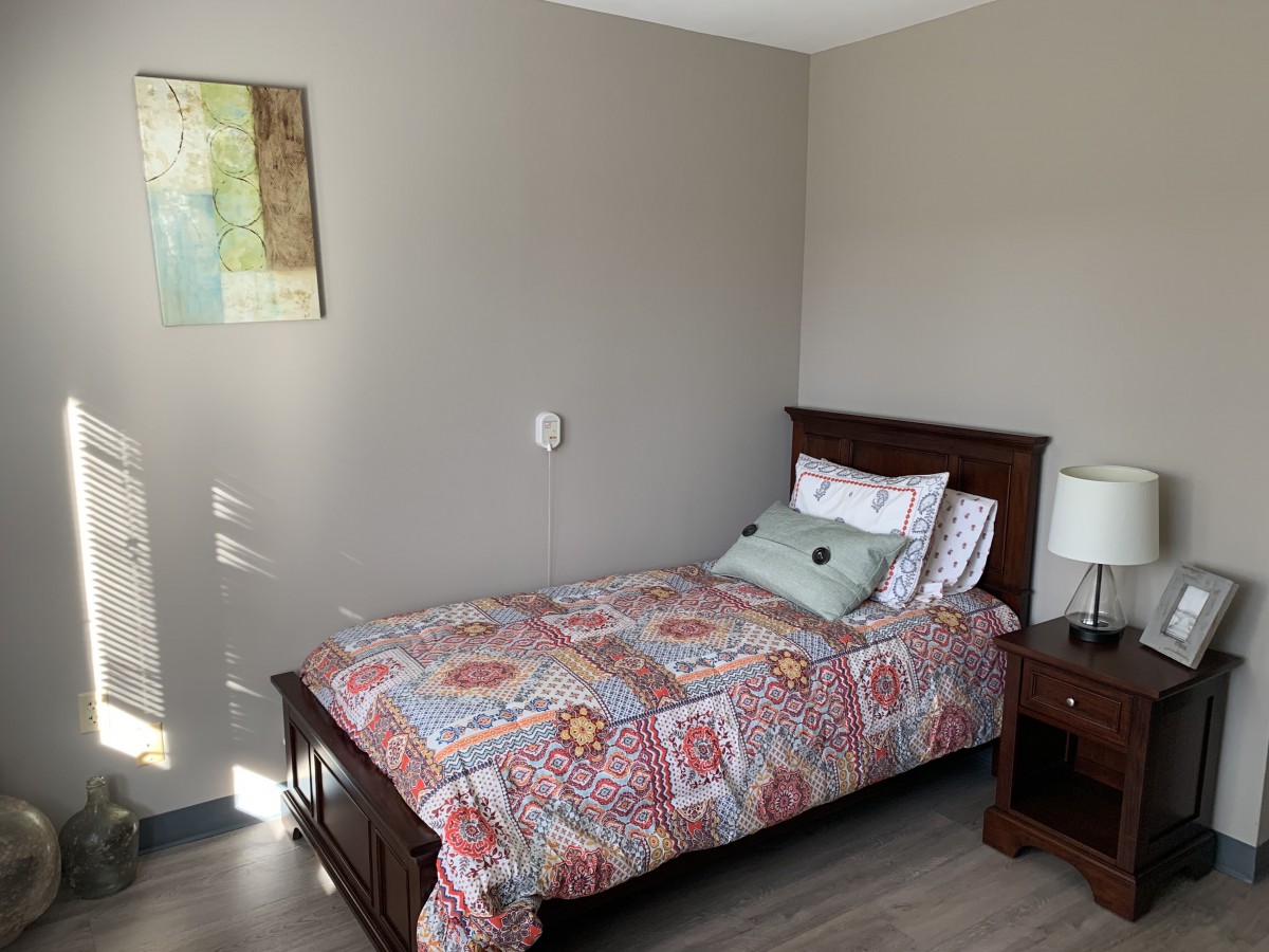 A cozy bedroom with a single bed featuring colorful bedding, a pillow, and a nightstand with a lamp.