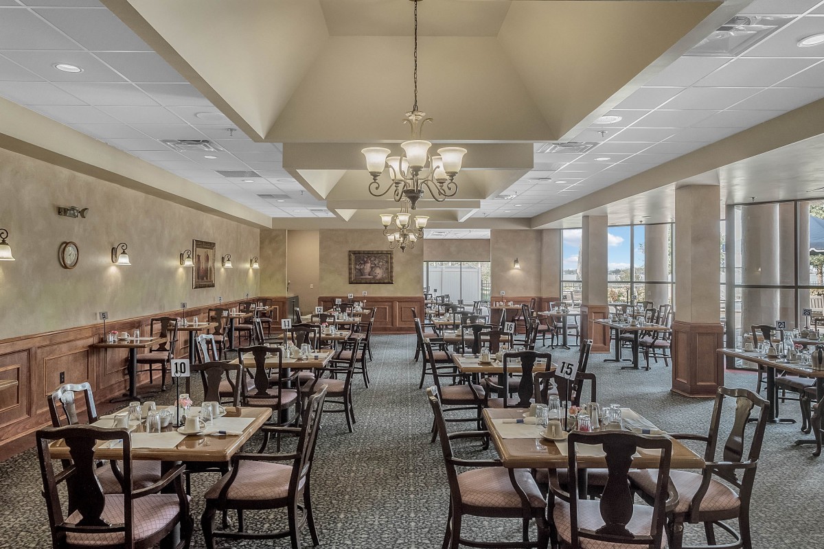 A spacious and elegantly decorated restaurant dining room with neatly arranged tables and chairs under large chandeliers.