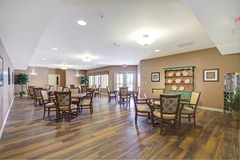 A spacious and well-lit dining room with several tables and chairs arranged on wooden flooring.