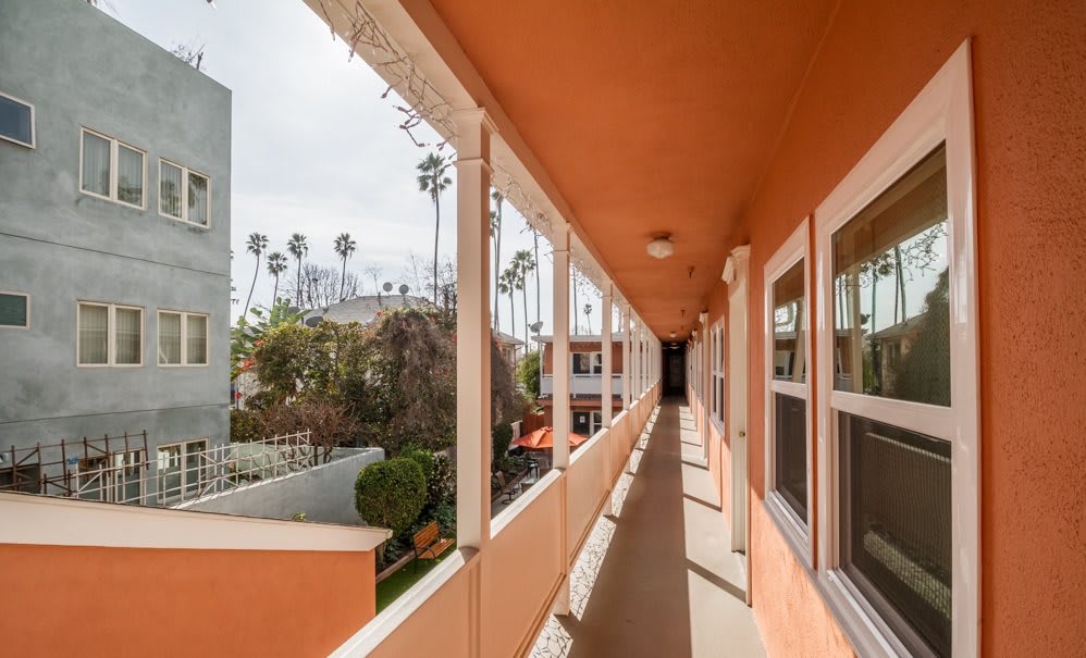 A view down an exterior corridor of a vibrant orange apartment complex with palm trees in the background.