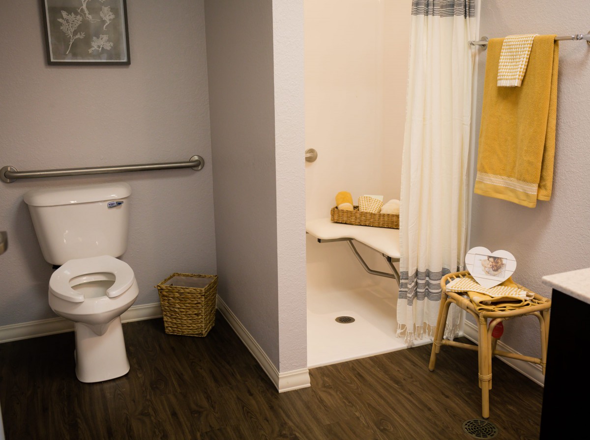 A modern bathroom featuring a toilet, shower area with a seat, and neatly arranged towels.