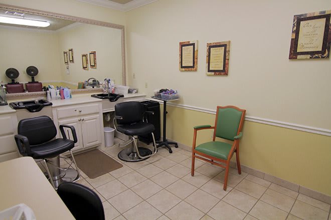 An empty salon interior featuring a barber chair, mirror, counter, and seating area.