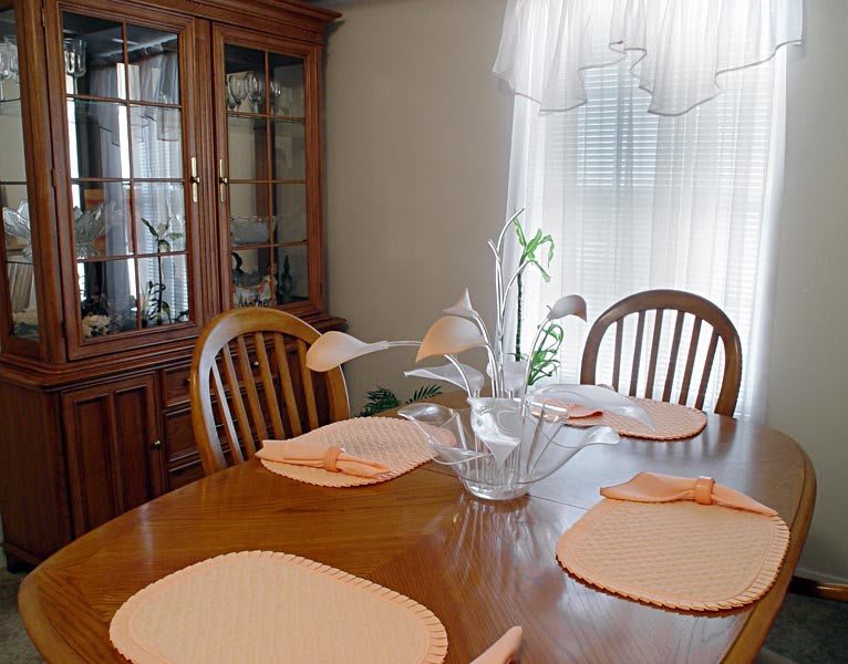 A cozy dining room with a wooden table set for four, featuring placemats and a vase with flowers.