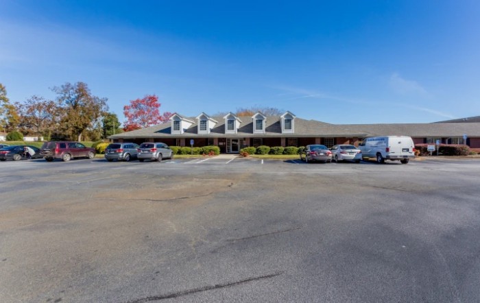 A wide view of a building with a parking lot in front, featuring several cars under a clear blue sky.