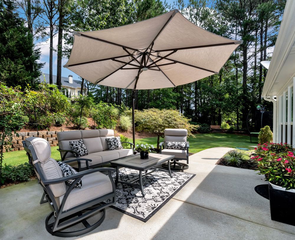A cozy outdoor patio setup with chairs, a table, and a large umbrella under a sunny sky.