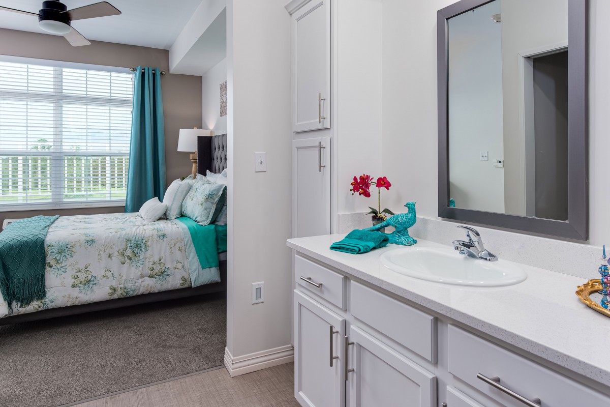 A modern bedroom with an adjoining bathroom featuring white cabinets and turquoise accents.