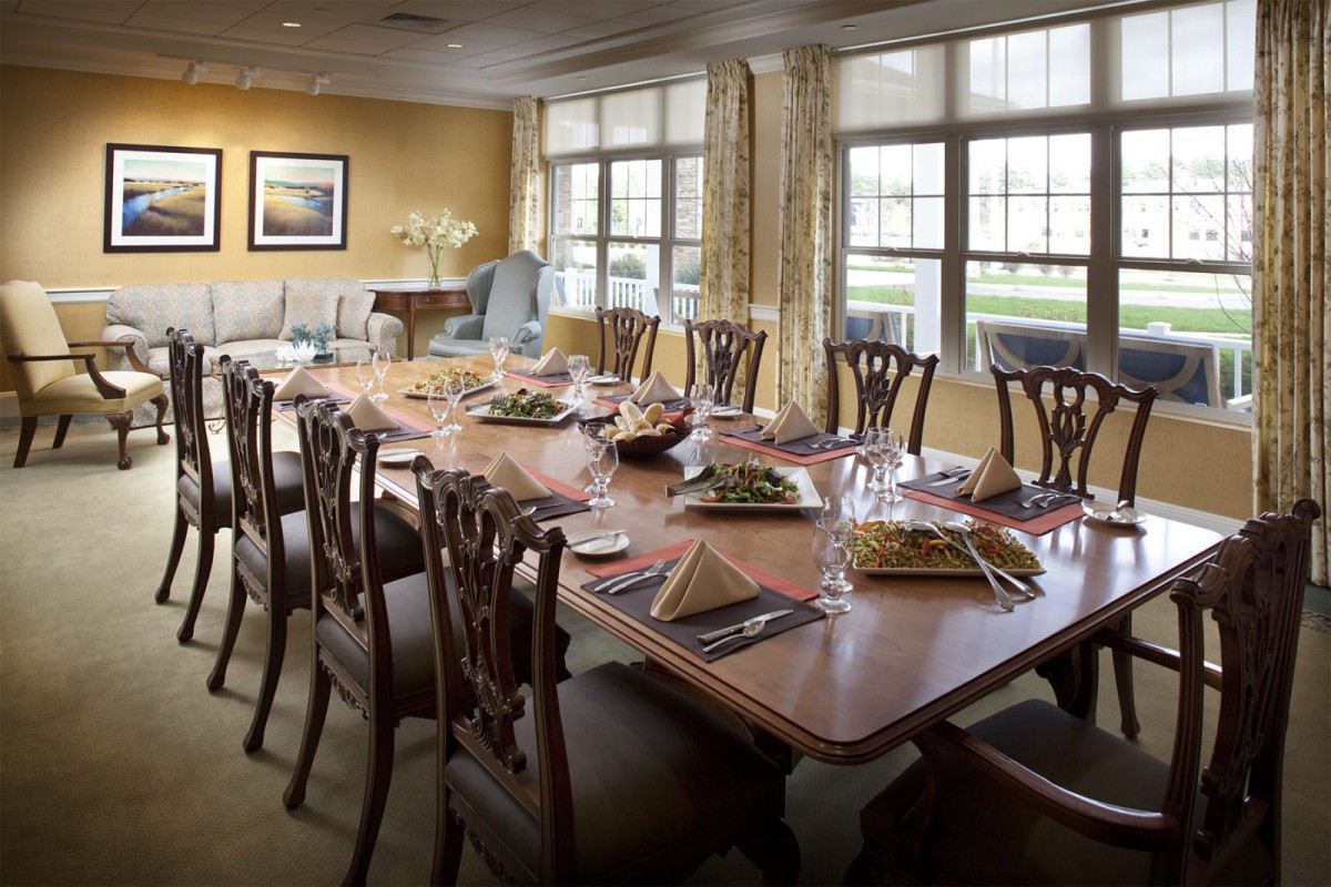 A well-set dining room table prepared for a meal, surrounded by elegant chairs and illuminated by natural light from large windows.