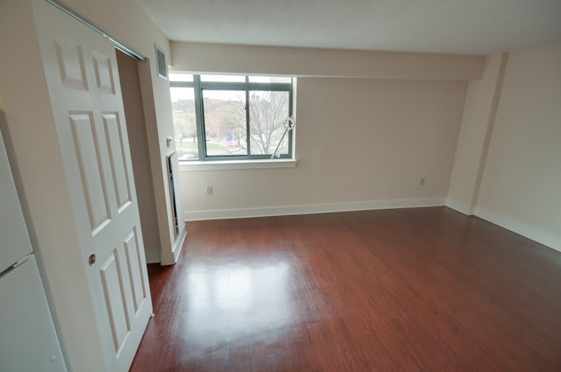 An empty room with hardwood flooring and a window allowing natural light.