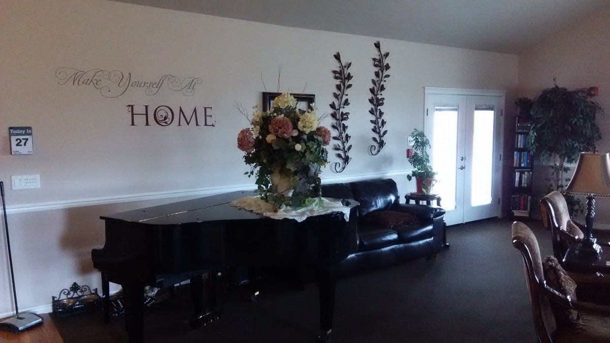 A cozy living room with a piano, floral arrangement, and comfortable seating.