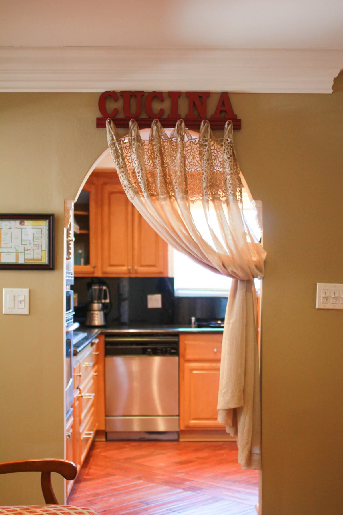 A cozy kitchen view through a decorated archway with curtains.