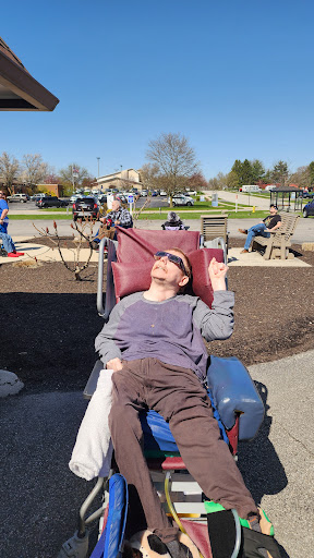 A person enjoying the sunny day in a park, relaxing on a comfortable chair.