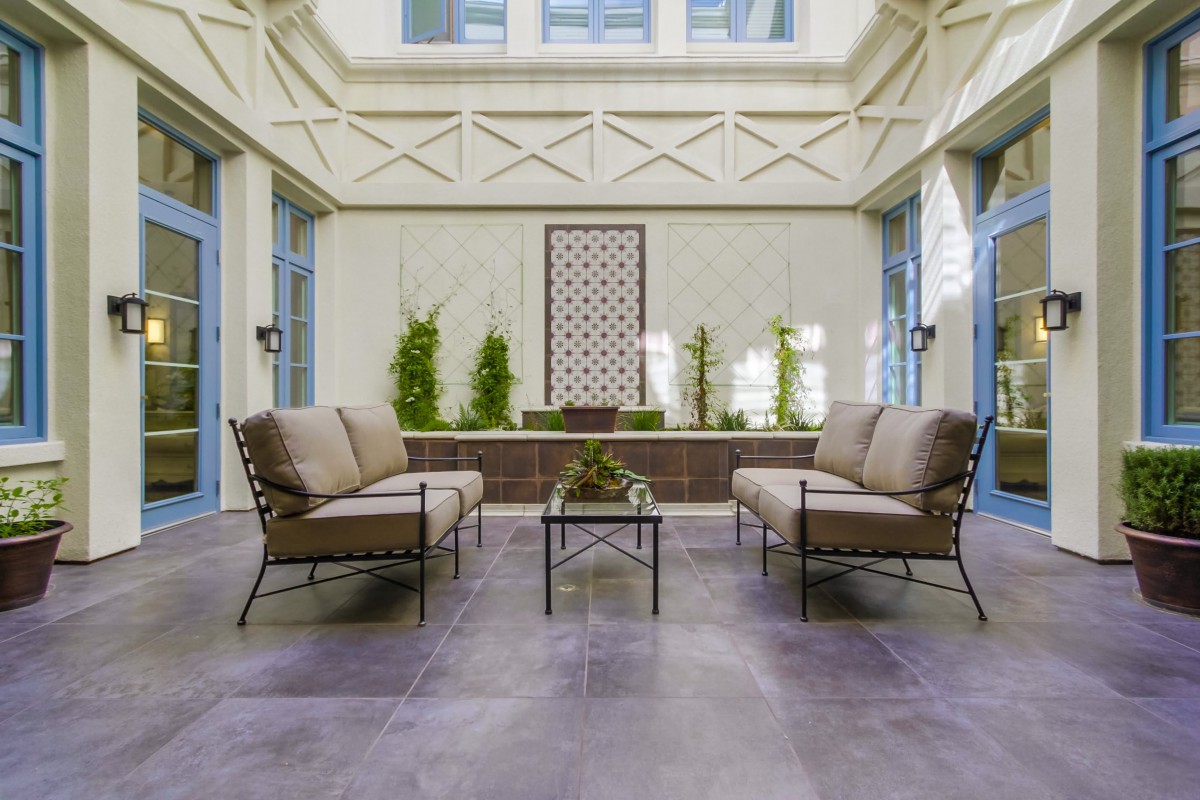 A modern outdoor patio with comfortable sofas and a coffee table, surrounded by plants.