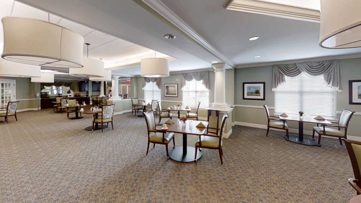 A spacious and elegant dining room with neatly arranged tables and chairs, soft lighting, and large windows.