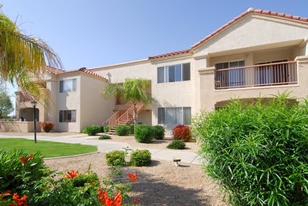 A sunny view of an apartment building surrounded by lush landscaping.