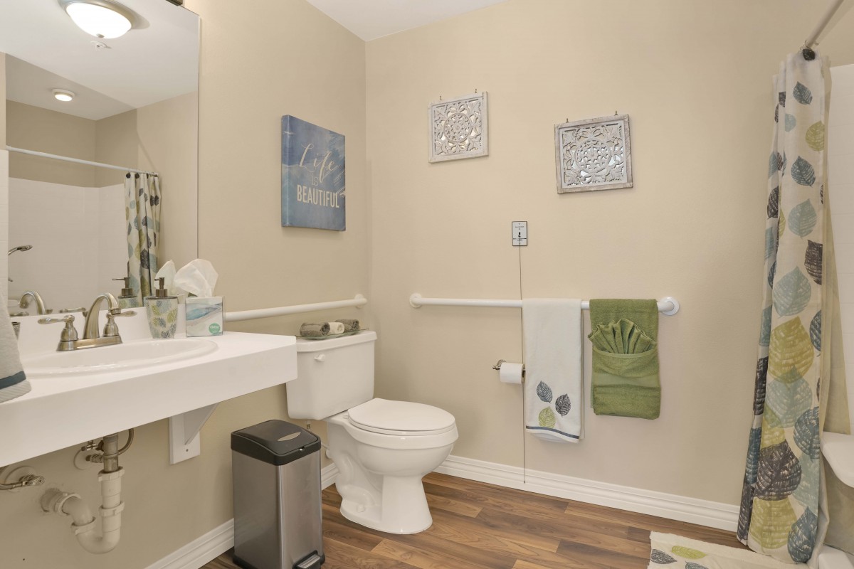 A modern bathroom with a toilet, sink, and wall art, featuring neutral tones and green towels.