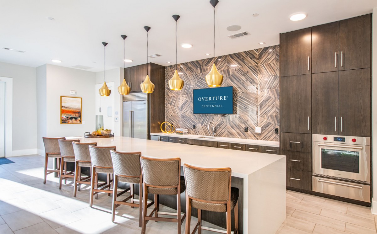A modern kitchen interior with a sleek countertop, gold pendant lights, and high chairs.