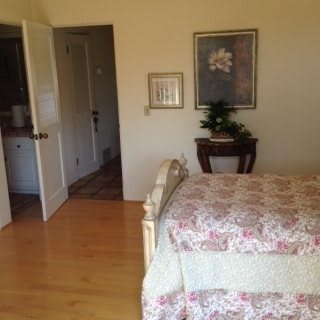 A cozy bedroom with a floral bedspread, decorative paintings on the wall, and a small plant on a table.