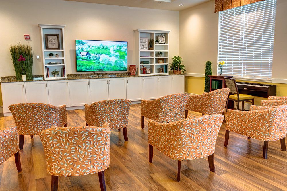 A cozy living room with patterned chairs facing a large television, surrounded by modern decor and shelves.