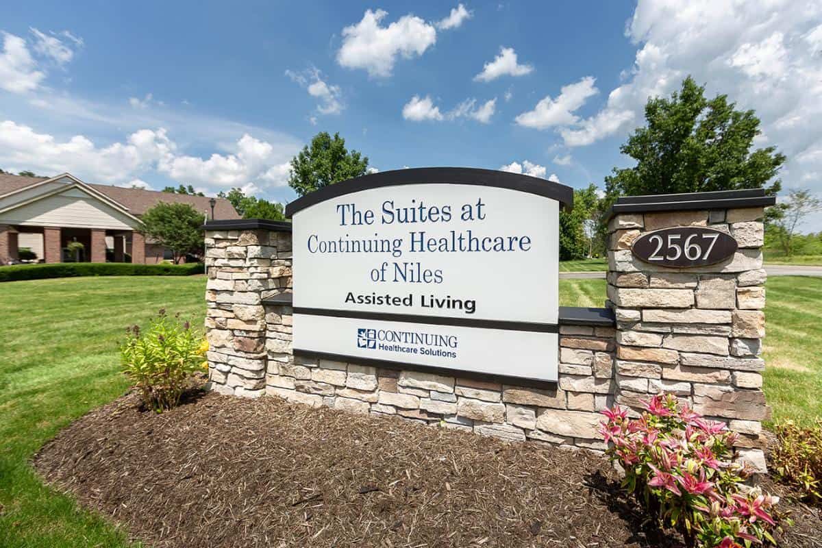 A sign for The Suites at Continuing Healthcare of Niles set outdoors against a blue sky.