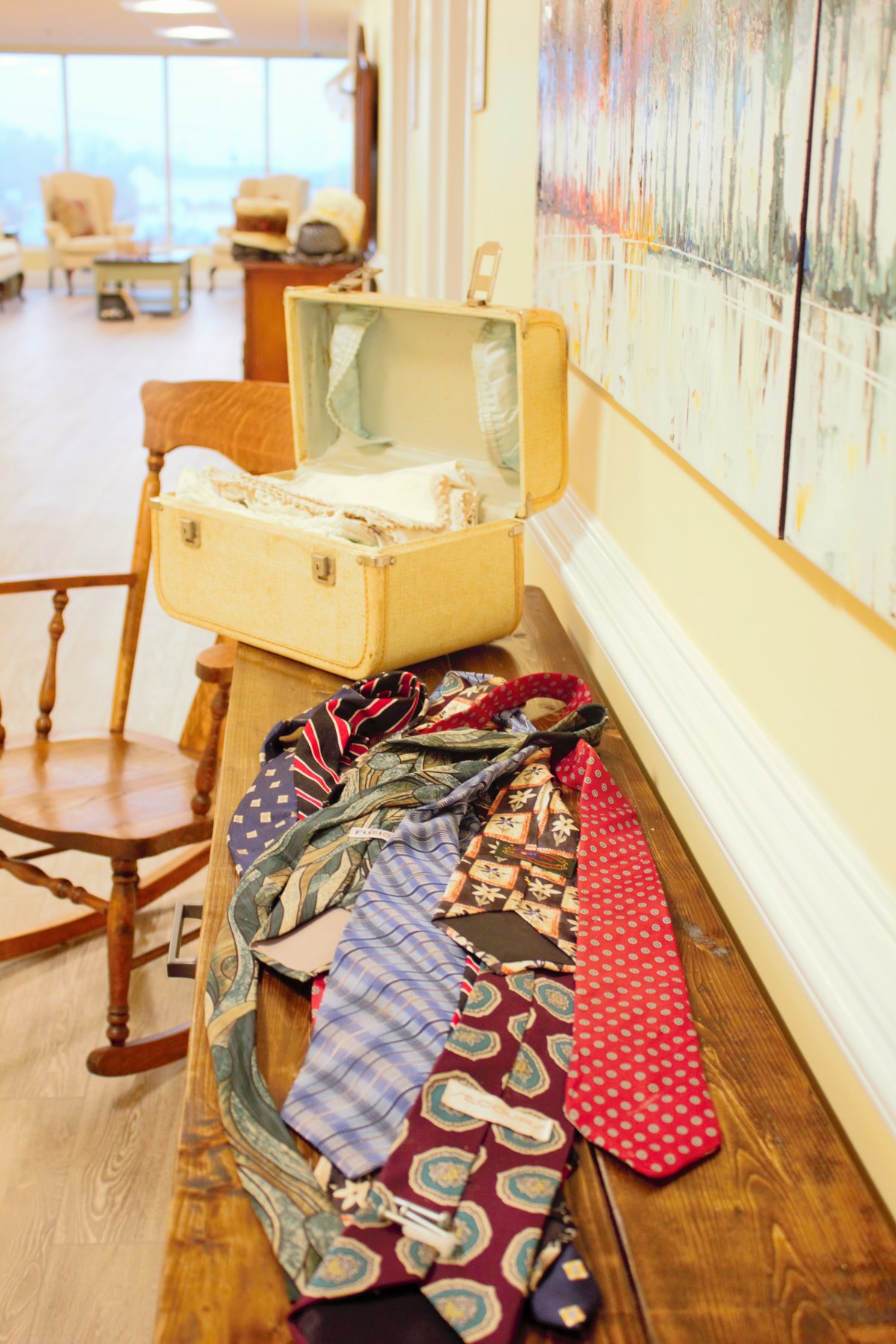 A vintage suitcase sits open on a wooden shelf, with an assortment of colorful neckties draped beside it.
