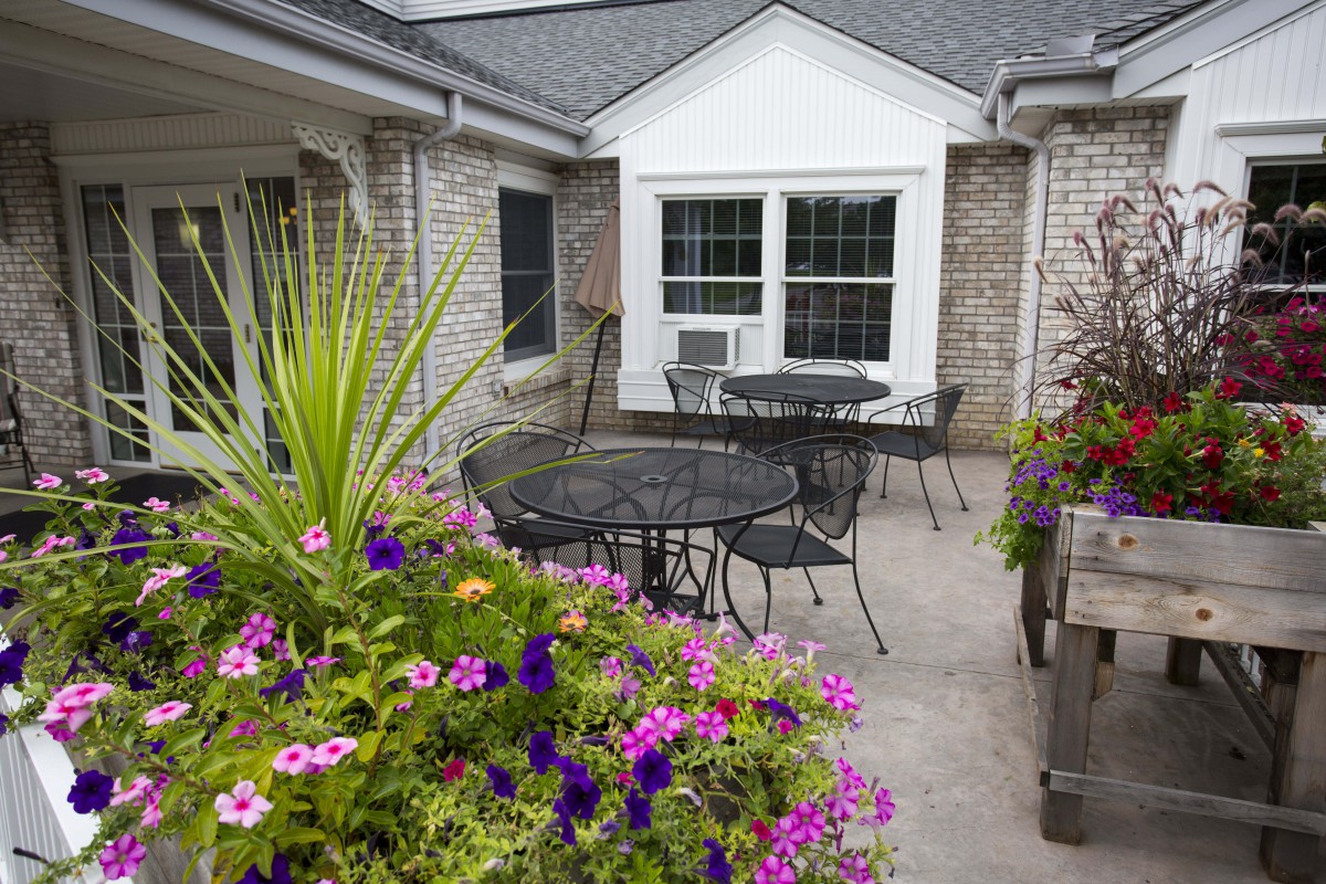 A cozy patio with colorful flowers, tables, and chairs.