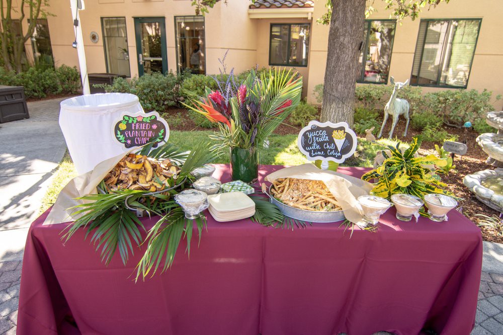 A beautifully decorated outdoor food table with a tropical theme, featuring colorful fruits and foliage.