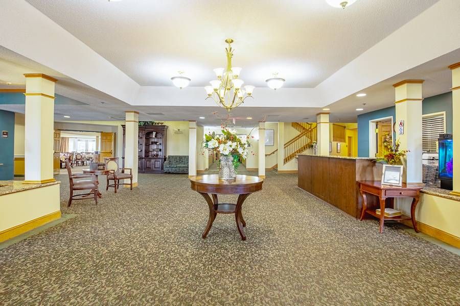 A well-lit lobby with elegant decor, featuring a central table adorned with flowers and a chandelier overhead.