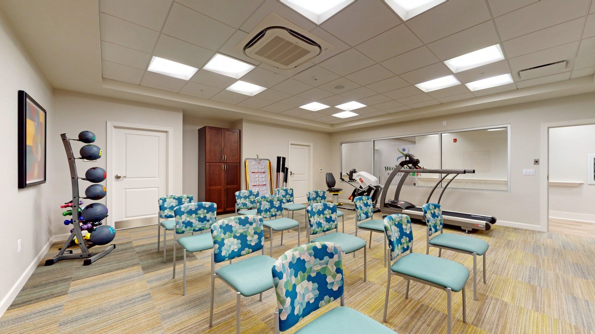 A multi-purpose room with floral-patterned chairs and fitness equipment.