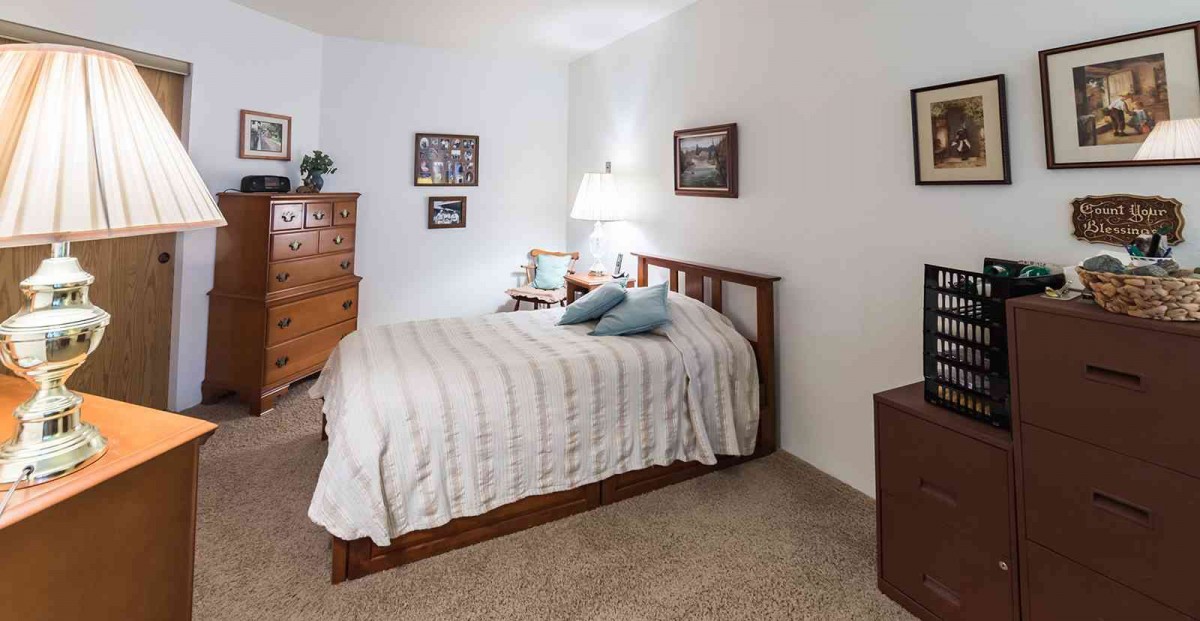 A cozy bedroom with a wooden bed, dresser, and soft lighting.