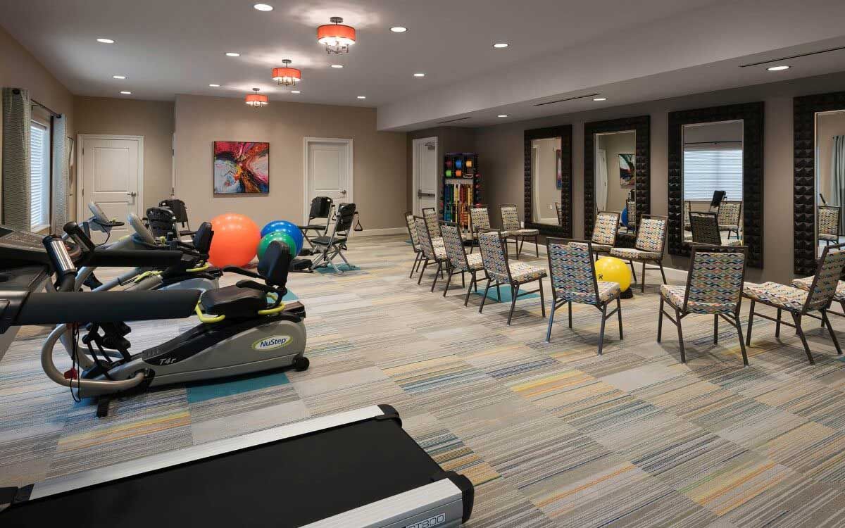 A spacious gym area equipped with exercise machines, therapy balls, and chairs for fitness activities.