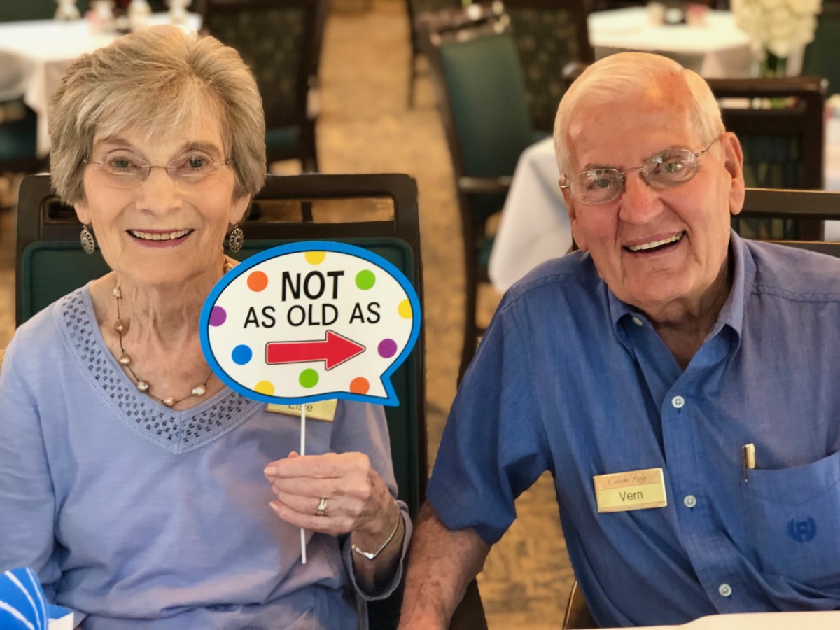 An elderly couple enjoying a celebration, holding a humorous sign.