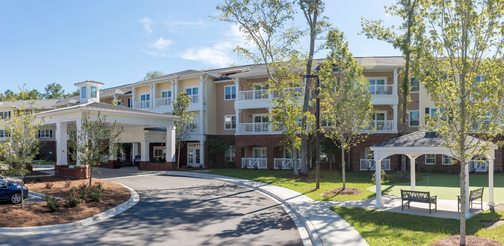 A modern residential building with a welcoming entrance, surrounded by trees, under a clear blue sky.