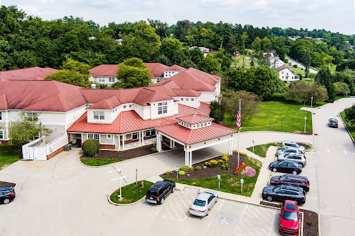 An aerial view of a hotel with a red roof, surrounded by greenery and parked cars.