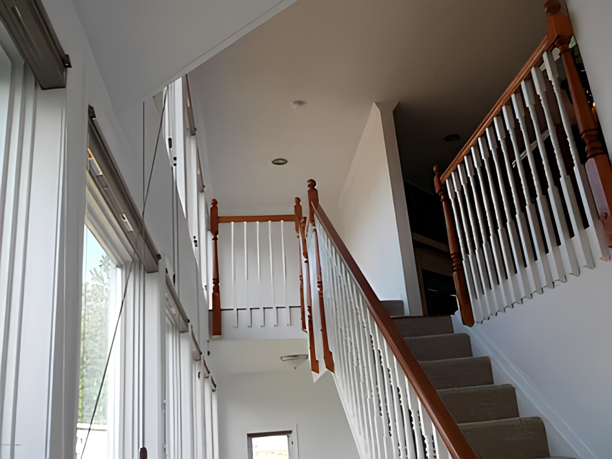 A well-lit staircase with wooden railings next to large windows.