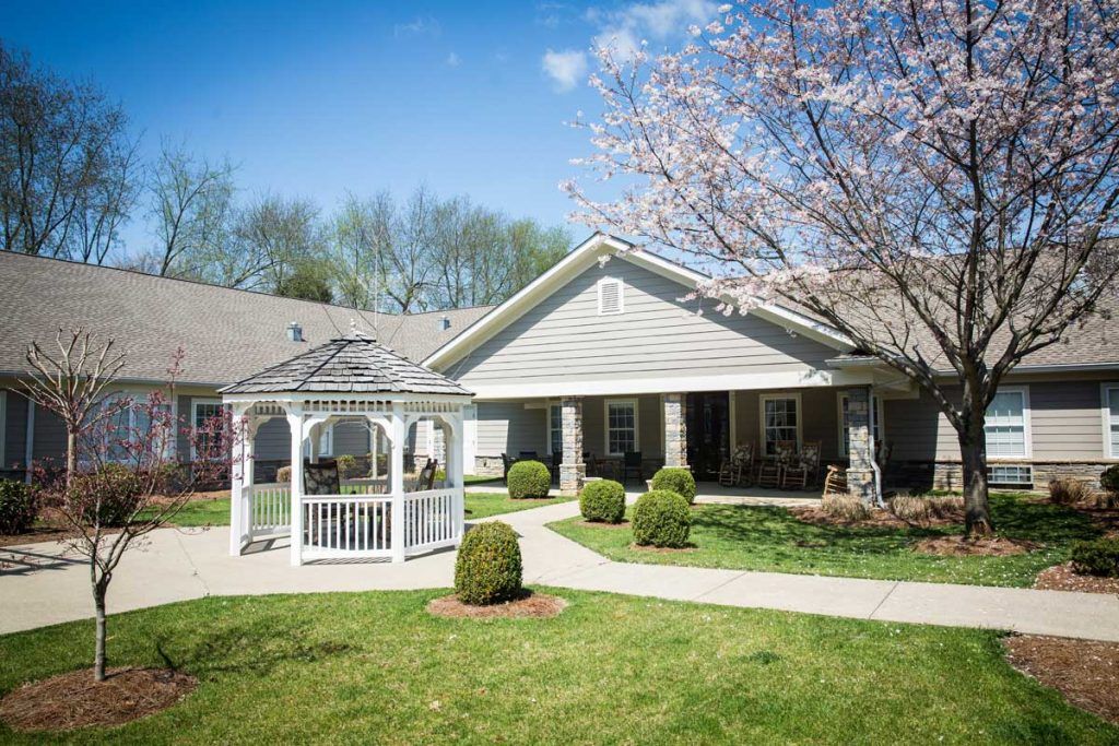A pleasant house with a white gazebo and manicured lawn surrounded by trees in full bloom.