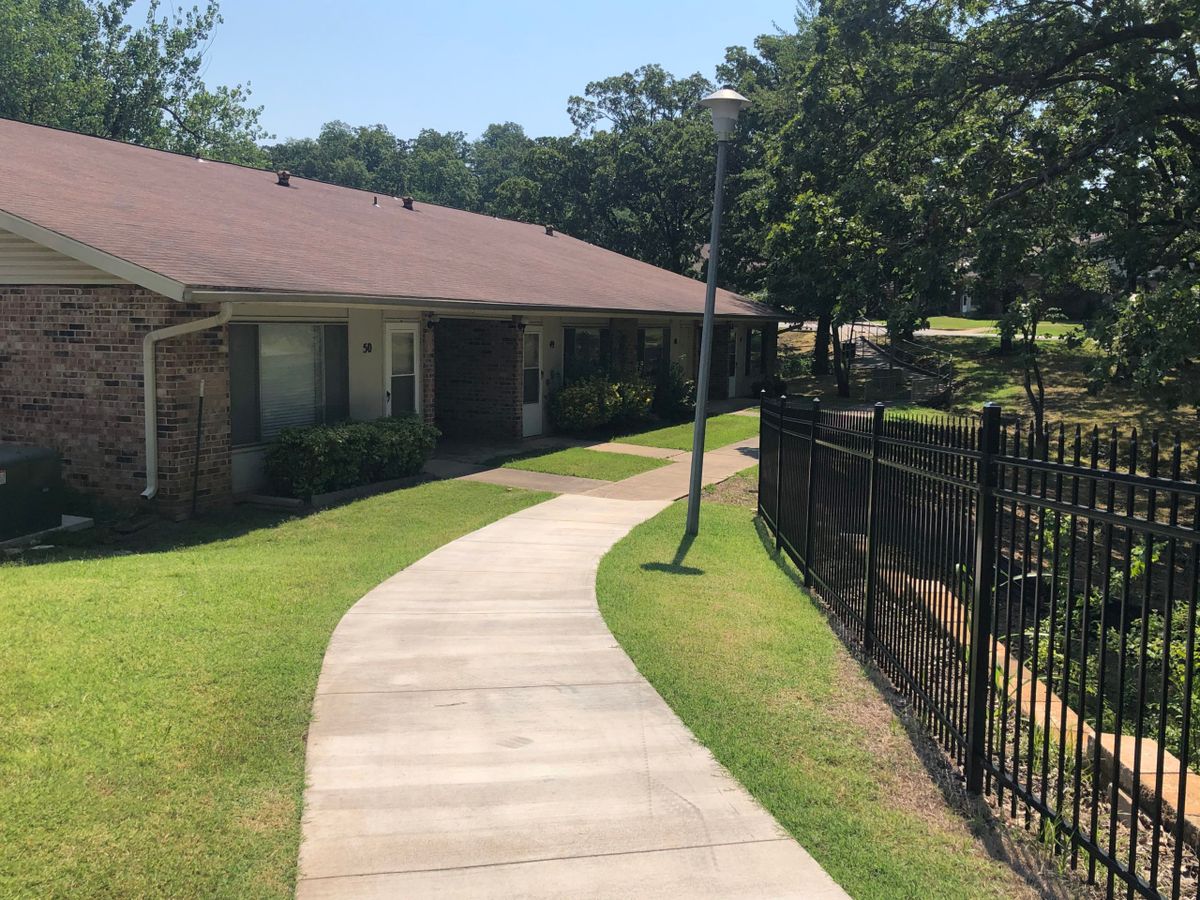 A sunny day with a sidewalk leading past a building and fenced area.