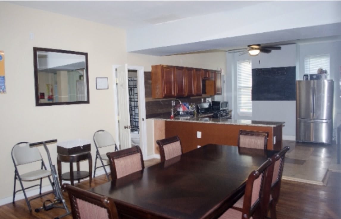 A dining room with a dark wooden table and chairs, adjoining an open-plan kitchen.