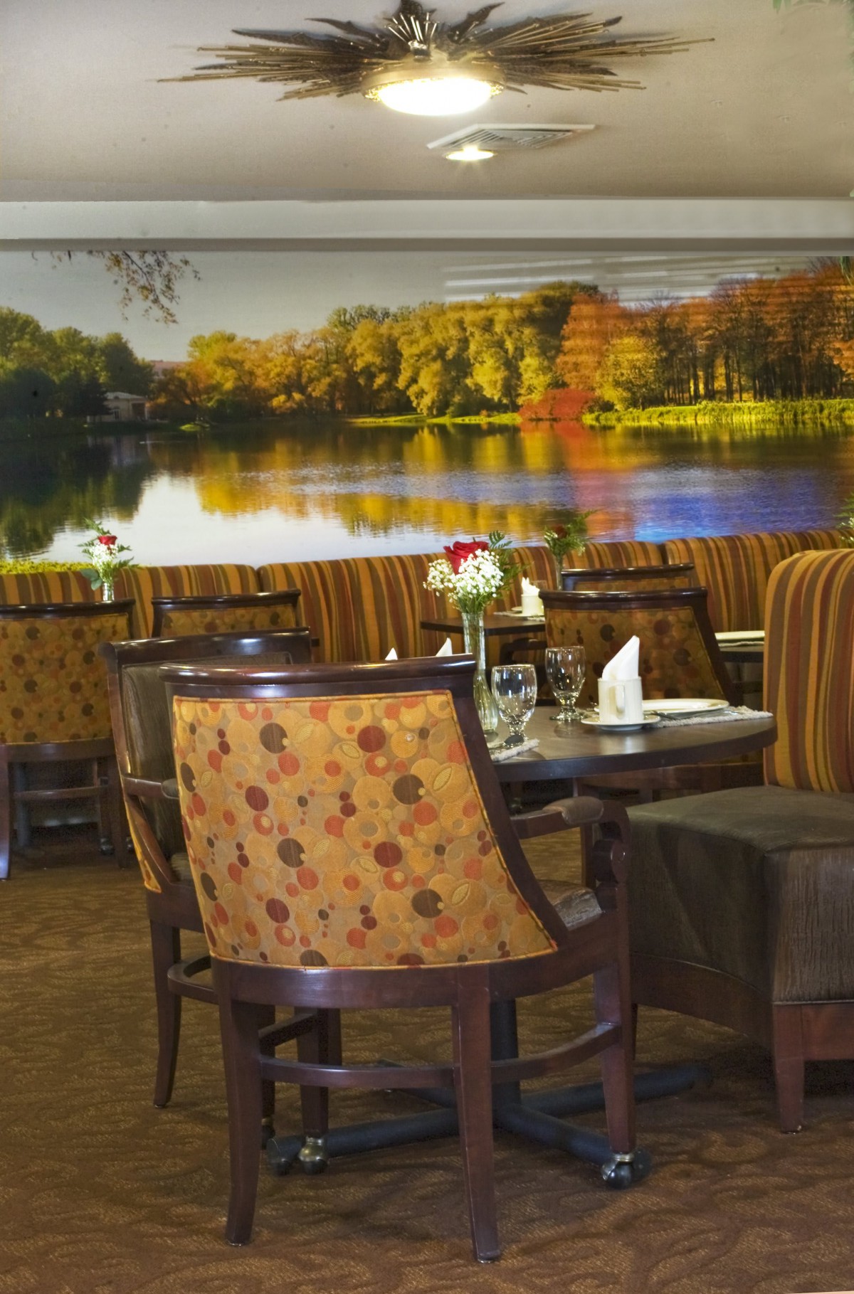 A cozy restaurant dining area featuring comfortable seating and a scenic wall mural of a lake.