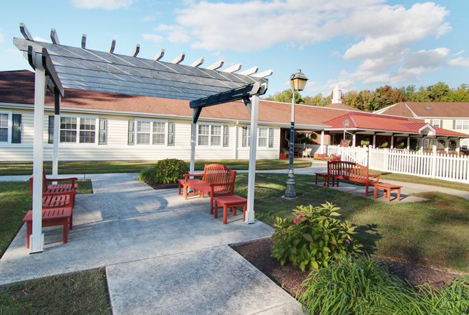 A tranquil garden setting with a pergola, pathways, and seating adjacent to a building.