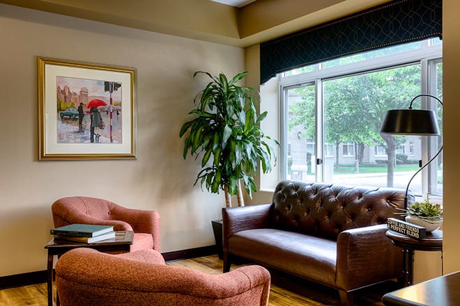 A cozy living room with a sofa, armchair, and a large window letting in natural light.
